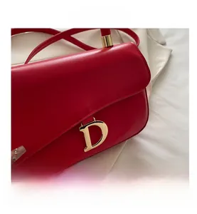 Détail d'un sac en cuir rouge avec une grande boucle métallique dorée en forme de lettre D