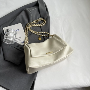 Creamy white pebbled leather crossbody tote bag with gold chain strap on grey blazer