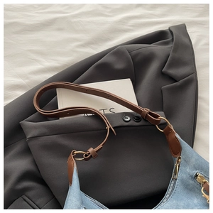 Detail of blue denim tote bag with brown leather strap on a grey blazer