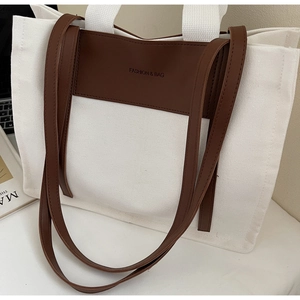 Canvas and brown leather tote bag detail with Fashion & Bag embossed logo on the desk