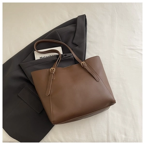 Détail d'un sac cabas marron avec sangle réglable et boucle dorée sur un blazer gris