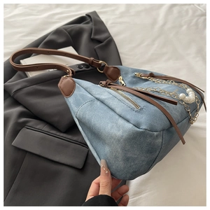 Detail of blue denim tote bag featuring golden chain and large pearl accents on dark blazer