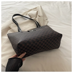 Detail of large tote bag with brown M-pattern jacquard and black leather handles
