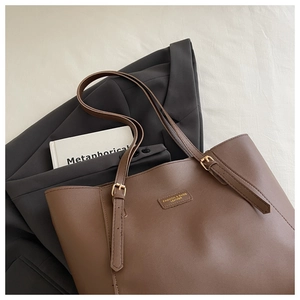 Sac fourre-tout en cuir marron avec boucles dorées et bandoulières réglables sur fond chic