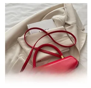 Détail du sac en cuir rouge avec boucle D dorée posé sur une veste blanche