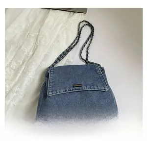 Detail of blue denim shoulder bag with golden hardware and chain strap on white background