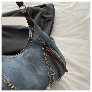 Detail of blue denim shoulder bag with brown leather straps and gold pearl charms