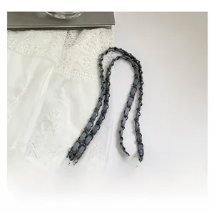Detail of blue denim shoulder strap woven with dark grey matte metal chain link