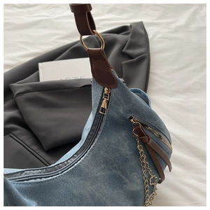 Detail of light blue denim crescent bag with brown leather strap and gold hardware accents