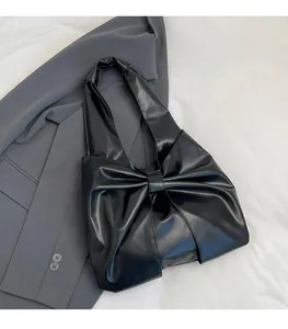 Détail du sac en similicuir noir avec un grand nœud décoratif et bandoulière intégrée