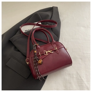 Detail of burgundy vintage shell bag with gold buckle and stylish charm on grey suit
