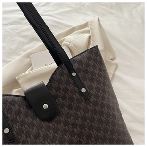 Detail of a large tote bag with brown M-pattern monogram and black leather straps