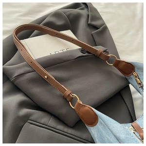 Detail of light blue denim hobo bag with brown leather strap and gold hardware accents