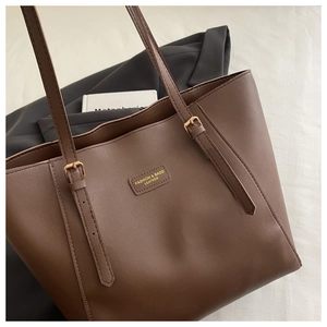Détail d'un sac cabas marron avec un patch en cuir et une boucle dorée réglable