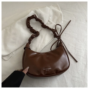 Detail of dark brown leather crescent bag with ruched handle and ribbon bow accent