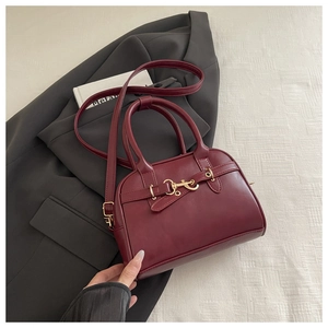 Close-up of deep red leather satchel with golden horsebit buckle and adjustable strap