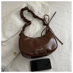 Detail of dark brown crescent bag with pleated shoulder strap and brand lettering