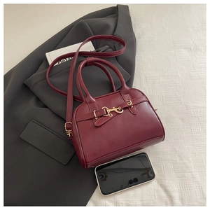Red Boston bag with gold horsebit hardware and phone for size reference on a blazer