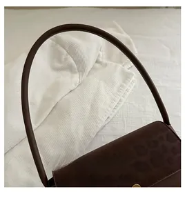 Detail of leopard print suede texture with round gold buckle and slim handle on brown bag
