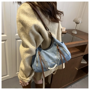 Detail of denim shoulder bag featuring pearl charms and gold chain strap accents