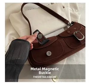 Detail showing the magnetic metal clasp closure on a brown suede underarm bag