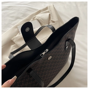 Close-up of brown tote bag with M-pattern, zipper closure and magnetic leather flap