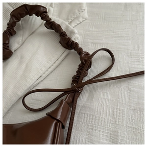 Detail of dark brown glossy shoulder bag with pleated strap and bow accent