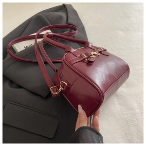 Macro detail of wine red leather handbag with gold metal clasp on grey fabric background