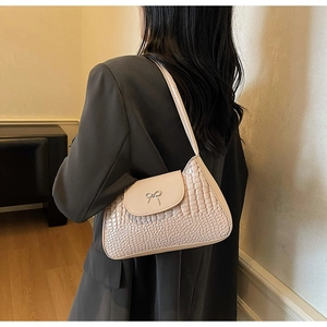 Close-up of beige crocodile pattern handbag with silver bow detail on the shoulder