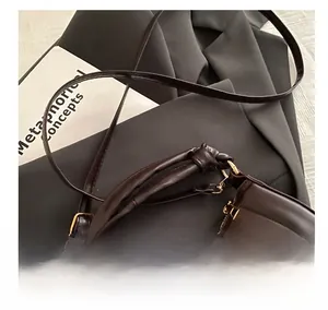 Detail of a dark brown leather bag with a unique knot handle and gold 'BAGS' lettering