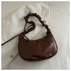 Top view of dark brown crescent bag with ruffled handle on white corduroy texture