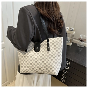 Close-up of stylish white tote bag with M-pattern print and slim black leather strap
