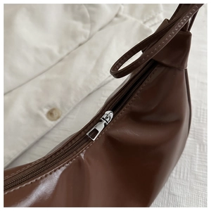 Detail of silver metal zipper and dark brown leather texture on crescent shoulder bag