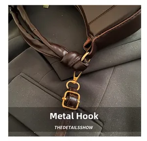 Detail of a dark brown leather handbag featuring a gold hardware hook and knotted strap design