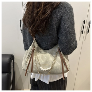 Detail of trendy crossbody bag with pearl strap, gold chain, and faux leather texture