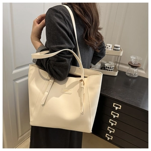 Détails des bandoulières réglables et de l'écusson sur un sac cabas blanc crème
