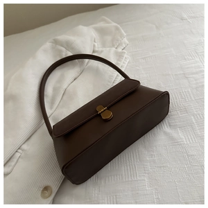 Close-up of a vintage dark brown baguette bag with matte gold rotary buckle on white fabric