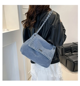 Detail of blue denim shoulder bag with metal chain strap worn on a stylish black leather jacket