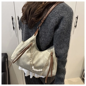 Detail of grey-green tote bag featuring pearl chain, tassels, and brown leather straps