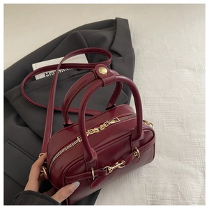 Detail view of burgundy faux leather handbag with gold horsebit and adjustable strap