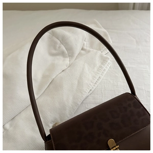 Detail of dark coffee baguette bag with leopard print flap and golden metal buckle