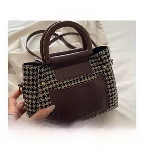 Detail view of the houndstooth pattern fabric and coffee brown leather handles on tote bag