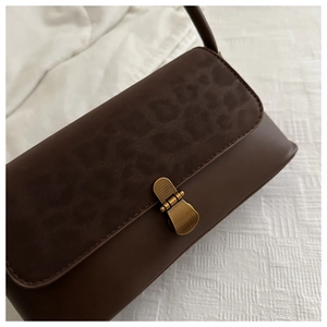 Close-up of vintage baguette bag with leopard print flap and gold clasp on white fabric
