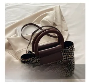 Detail showing the classic houndstooth pattern and leather handles of the crossbody bag