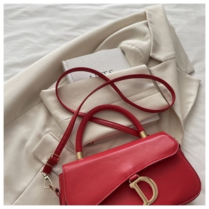 Détail du sac selle rouge avec boucle en D dorée sur un blazer beige et un livre