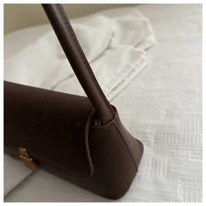 Detail of brown leather shoulder bag featuring gold buckle and precise stitching accents