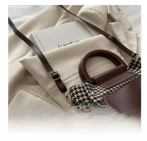 Close-up of brown leather shoulder strap with golden metal buckle on houndstooth bag