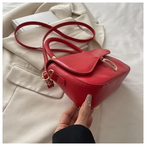 Détail d'un sac à main en cuir rouge avec boucle dorée en D sur blazer beige