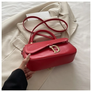 Détail du sac selle en cuir rouge avec logo D doré sur un blazer beige élégant