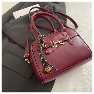 Detail of burgundy handbag with gold horsebit hardware and woven charm on gray blazer
